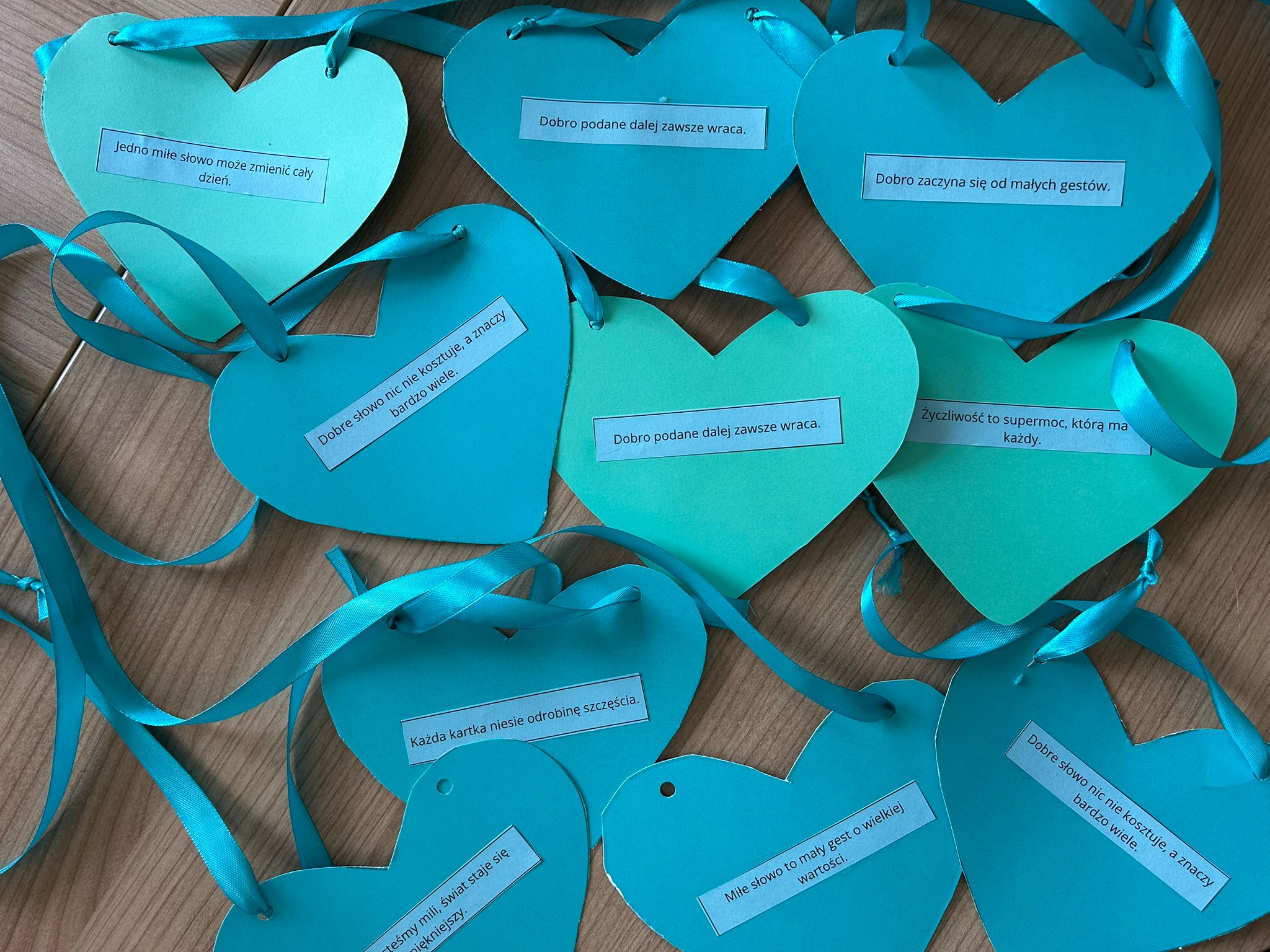 Zdjęcie przedstawia papierowe niebieskie serca z optymistycznymi sentencjami i błękitnymi wstążkami.
