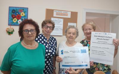 Wnętrze świetlicy wiejskiej w Paczkowie. Cztery seniorki pozują do zdjęcia trzymając plakaty projektowe.