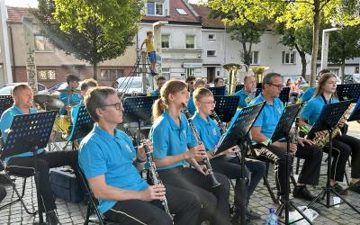 Kilkanaścioro muzyków ze Swarzędzkiej Orkiestry Dętej koncertują na Placu Niezłomnych w otoczeniu liściastych drzew i kamiennic. Na pierwszym planie muzycy grający na fletach prostych.