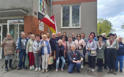Zdjęcie przedstawia dwadzieścia pięć osób - uczestniczek i uczestników gry terenowej stojących przed wejściem do siedziby Dziennego Domu Senior Wigor.
