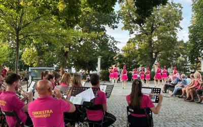 Letni Koncert na Plantach Swarzędzkiej Orkiestry Dętej. Na pierwszym planie siedzący członkowie orkiestry, w tle zebrani słuchacze i tańczące mażoretki.
