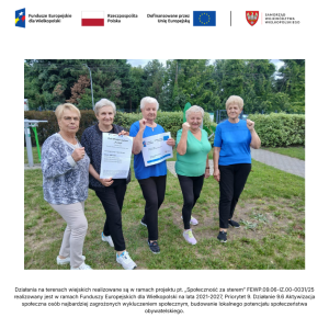 Pięć seniorek, uczestniczek zajęć, stoi na trawniku przed świetlicą wiejską w Jasinie. Dwie z nich pokazują plakaty projektowe.