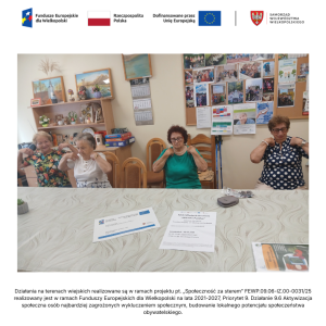 Zajęcia ruchowe w Paczkowie. Cztery seniorki siedzą za stołem i kręcą ramionami trzymając dłonie na barkach.