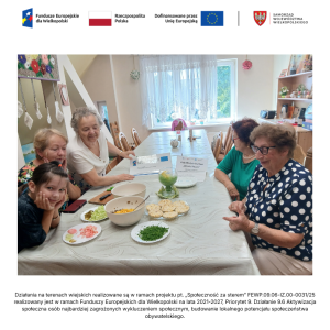 Wnętrze świetlicy wiejskiej w Paczkowie. Przy długim stole, na którym stoją produkty, siedzą cztery seniorki i jedna dziewczynka.