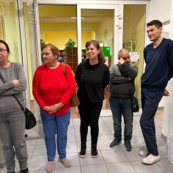 Uczestnicy Środowiskowego Domu Samopomocy i zaproszeni goście stoją na korytarzu Biblioteki Publicznej w Swarzędzu na osiedlu Czwartaków.