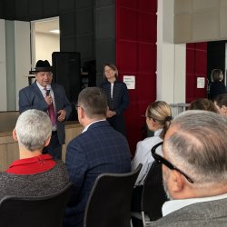 Mężczyzna w kapeluszu, przedstawiciel społeczności romskiej w Swarzędzu, mówi do mikrofonu, uczestnicy konferencji słuchają jego wystąpienia.