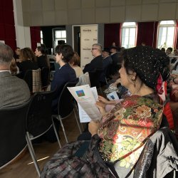 Widok publiczności uczestniczącej w konferencji. Na pierwszym planie Romka w ozdobnej chustce na głowie, pięknej chuście na ramieniu i długiej spódnicy.