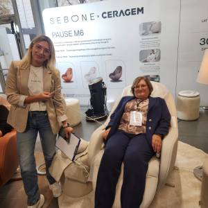 Wnętrze hali targowej. Druga ze swarzędzkich laureatek sprawdza działanie fotela z opcją masażu. Obok niej stoi instruktorka trzymająca pilota.