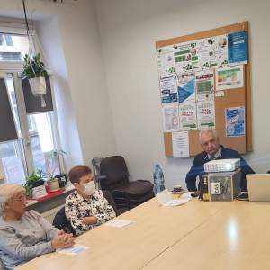 Zdjęcie przedstawia doktora Suworkina siedzącego za stołem i dającego prelekcję. Przy stole siedzą również seniorzy - uczestnicy warsztatu.