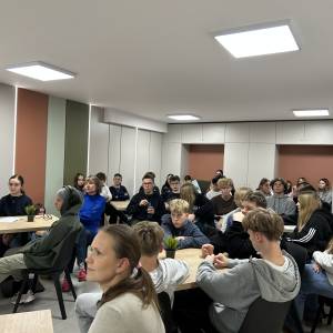 Zdjęcie przedstawia spotkanie z uczniami w sprawie utworzenia Rady Młodzieży. Kilkudziesięcioro uczniów siedzi przy stolikach w świetlicy i słucha.