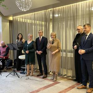 Wigilia w Eurohotelu. Przemawia przewodnicząca rady miejskiej. Obok niej widać zespół muzyczny, dyrektor Centrum, burmistrza, księdza i wiceburmistrza.