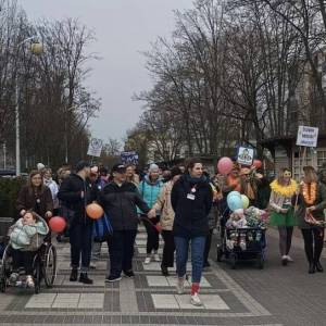 Marsz Kolorowej Skarpetki. Na zdjęciu widać kilkadziesiąt osób z balonami i transparentami, idących po deptaku na osiedlu Czwartaków.