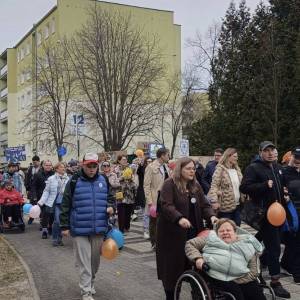 Marsz Kolorowej Skarpetki. Na zdjęciu widać kilkadziesiąt osób z balonami i transparentami, idących po deptaku na osiedlu Kościuszkowców.