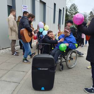 Plac przed Ośrodkiem Terapii i Rehabilitacji przy ulicy Zamkowej. Piotr Śliwiński siedzący na wózku inwalidzkim śpiewa do mikrofonu utwór Sto.