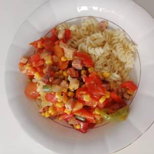 Zdjęcie przedstawia zbliżenie na biały głęboki talerz wypełniony makaronem w kształcie świderków z jednej strony i warzywami z boczkiem z drugiej strony.