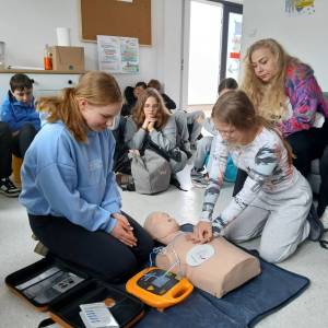 Gra miejska pod tytułem Ratujemy, bo umiemy. Na podłodze klęczą dwie dziewczynki. Jedna z nich uciska fantoma. Druga patrzy na sprzęt AED.