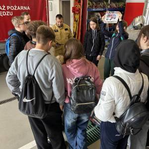 Wnętrze remizy Ochotniczej Straży Pożarnej w Swarzędzu. Grupa uczniów układa na podłodze układankę z dużych klocków. Wszystko obserwuje naczelnik.