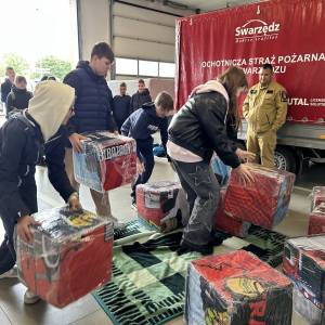 Wnętrze remizy Ochotniczej Straży Pożarnej w Swarzędzu. Grupa uczniów układa na podłodze układankę z dużych klocków. Wszystko obserwuje naczelnik.