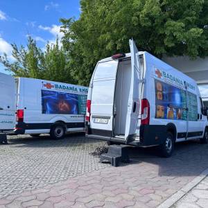 Na zdjęciu widać dwa duże busy diagnostyczne stojące na parkingu przy Centrum Usług Społecznych w Swarzędzu. W tle widać drzewa, błękit nieba i chmury.