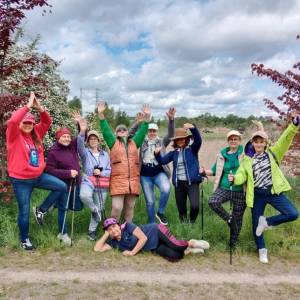 Grupa spacerowiczek nordic walking w Dolinie Cybiny. Każda z kobiet wykonuje pozę wyrażającą aktywność fizyczną. Jedna kobieta leży podparta na trawie.
