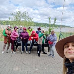 Selfie wykonane obok przystani nad Jeziorem Swarzędzkim. Widać twarz kobiety w kapeluszu trzymającej aparat, za nią grupa spacerowiczek, w tle jezioro.