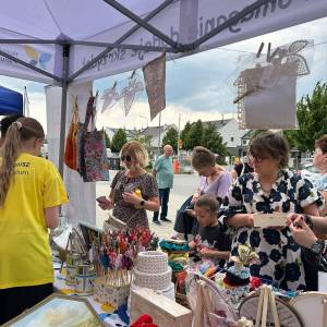Impreza pod tytułem Dbamy o mamy. Zdjęcie wykonane z wnętrza namiotu stoiska Hospicjum Palium. Zaciekawione uczestniczki imprezy oglądają ozdoby.
