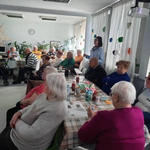 Dzienny Dom Senior Wigor. Kilkanaścioro seniorów słucha opowiadania wolontariuszki z Francji o Asteriksie i Obelliksie. 