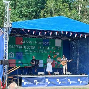 Scena dwudziestego pierwszego pikniku integracyjnego w Lisówkach. Trwa występ zespołu składającego się z wokalistki, gitarzysty i akordeonisty.
