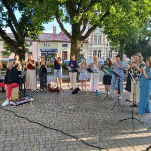 Swarzędzka Orkiestra Flażoletowa wykonuje utwór. Uwagę przyciąga artysta w czerwonych spodniach i białych butach siedzący i grający na cajonie. 
