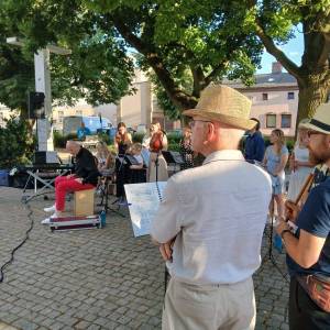 Letni koncert na Plantach. Chwila pomiędzy utworami. Dyrektor orkiestry Wojciech Wietrzyński opowiada publiczności o kolejnych melodiach.