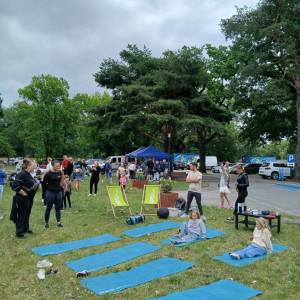 Na pierwszym planie na trawie widać stanowisko Well Fitness. W tle widać uczestników pikniku, niebieski namiot koła gospodyń wiejskich i zielone drzewa.