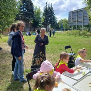 Ogród społeczny. Na zdjęciu widać przedszkolaki przygotowujące deser z owoców. Za nimi stoi dyrektor Centrum Usług Społecznych z dwiema pracowniczkami.