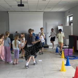 Wnętrze świetlicy w Garbach. Część dziewczynek bawi się w kręgu. Część uczestników chodzi lub stoi. Jedna dziewczynka skacze na skakance.