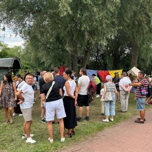 Zgromadzeni uczestnicy imprezy Piknik Trzech Pokoleń spędzają czas na trawie przy taborze cygańskim. 