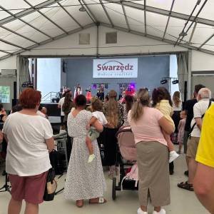 Zdjęcie wykonane w trakcie Pikniku Trzech Pokoleń. Na scenie występuje zespół cygański, a przed nią zgromadzony tłum widzów.