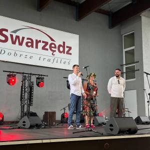 Na scenie wiceburmistrz Swarzędza, dyrektor Centrum Usług Społecznych w Swarzędzu i prowadzący imprezę. W tle sprzęt muzyczny i napis Swarzędz.
