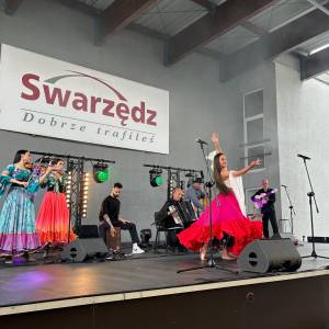 Występ zespołu cygańskiego na scenie nad Jeziorem Swarzędzkim. Dziewczyna tańczy w długiej kolorowej spódnicy.