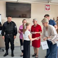 Zdjęcie ukazuje moment wręczenia nagrody i dyplomu jednej z zawodniczek przez dyrektor szkoły podstawowej numer dwa w Swarzędzu. Po prawej stronie dyrektor stoi troje przedstawicieli Centrum Usług Społecznych oraz dwoje strażaków.