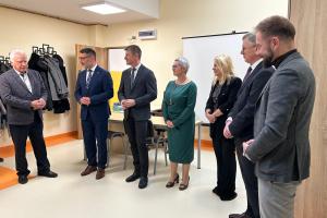 Zdjęcie przedstawia uroczystość otwarcia Klubu Rozwoju Cyfrowego i nowego mieszkania treningowego przy ulicy Wrzesińskiej w Swarzędzu. Na zdjęciu widać zaproszonych gospodarzy i gości stojących we wnętrzu głównej sali w Klubie Rozwoju Cyfrowego. Od lewej stoją: przemawiający Ryszard Dyzma - Przewodniczący Komisji Spraw Społecznych Rady Miejskiej w Swarzędzu, Tomasz Zwoliński - drugi zastępca burmistrza miasta i gminy Swarzędz, Grzegorz Taterka - pierwszy zastępca burmistrza, Agnieszka Maciejowicz - dyrektor Centrum Usług Społecznych w Swarzędzu, Katarzyna Kretkowska - członkini zarządu województwa wielkopolskiego, Marian Szkudlarek - burmistrz miasta i gminy Swarzędz oraz Grzegorz Grygiel - dyrektor Regionalnego Ośrodka Polityki Społecznej w Poznaniu.