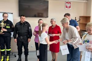 Zdjęcie ukazuje moment wręczenia nagrody i dyplomu jednej z zawodniczek przez dyrektor szkoły podstawowej numer dwa w Swarzędzu. Po prawej stronie dyrektor stoi troje przedstawicieli Centrum Usług Społecznych oraz dwoje strażaków.
