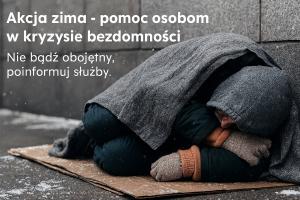 Zdjęcie przedstawia bezdomnego mężczyznę śpiącego na ośnieżonym kartonie położonym na chodniku. Mężczyzna jest przykryty kocem. Na głowie ma kaptur.