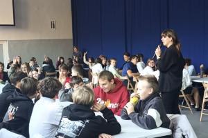 Zdjęcie przedstawia spotkanie z uczniami w sprawie utworzenia Rady Młodzieży. Jedna z prelegentek stoi pomiędzy uczestnikami i mówi do mikrofonu.