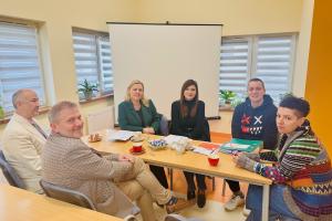 Zdjęcie przedstawia wnętrze klubu rozwoju cyfrowego w Swarzędzu. Przy stole siedzą trzy kobiety i trzech mężczyzn. Wszyscy patrzą w kierunku obiektywu.