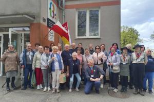 Zdjęcie przedstawia dwadzieścia pięć osób - uczestniczek i uczestników gry terenowej stojących przed wejściem do siedziby Dziennego Domu Senior Wigor.