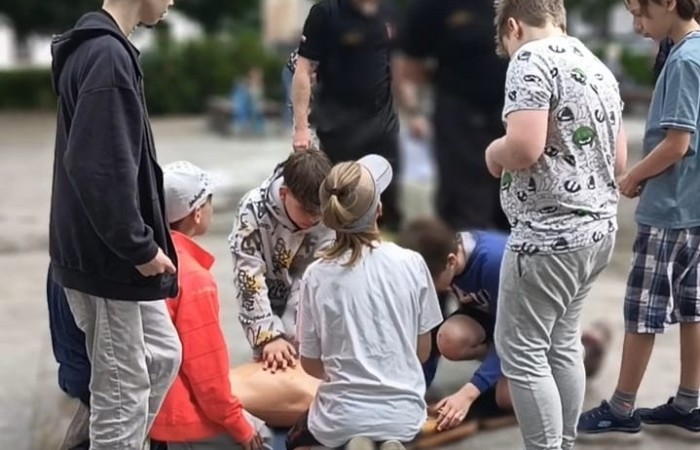 Na płycie placu Niezłomnych widać uczniów wykonujących na fantomie resuscytację krążeniowo-oddechową. Ich poczynania obserwuje dwóch strażaków.