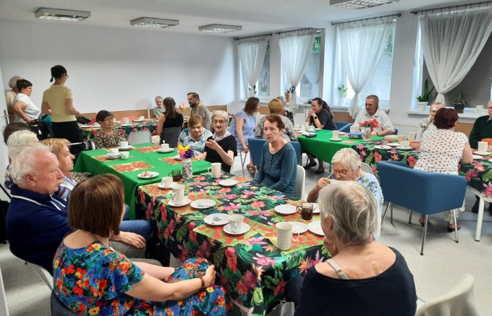 Główna sala Dziennego Domu Pomocy. Przy uroczyście ubranych stołach siedzą seniorzy, dyrekcja Centrum Usług Społecznych oraz pracownicy.