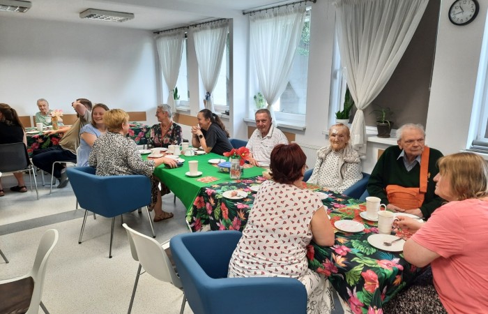 Główna sala Dziennego Domu Pomocy. Przy uroczyście ubranych stołach siedzą seniorzy, dyrekcja Centrum Usług Społecznych oraz pracownicy.