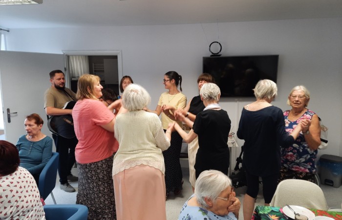 Pożegnanie Żuljet Żama w Dziennym Domu Pomocy. Pracownik Domu Rafał Wójtowicz gra na gitarze, a seniorki i Żuljet tańczą w kółku.