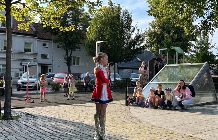 Koncert Swarzędzkiej Orkiestry Dętej na Plantach. Na pierwszym planie dziewczynka ubrana w  czerwoną krótką sukieneczkę i długie złote buty tańcząca z mażoretką.