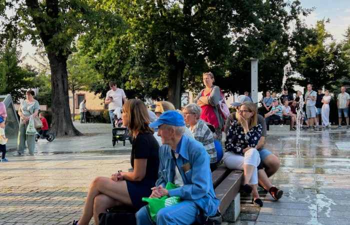 Koncert Swarzędzkiej Orkiestry Dętej na Plantach. Wśród liściastych drzew, na ławkach siedzą wsłuchani ludzie.